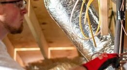 Worker looking at ductwork in an attic